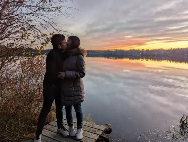 ggraph of Chris and Emily kissing on a dock at a lake at sunset